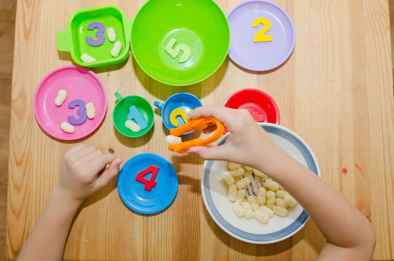 A child with sensory issues using tongs to count food during a feeding therapy session with a dietitian