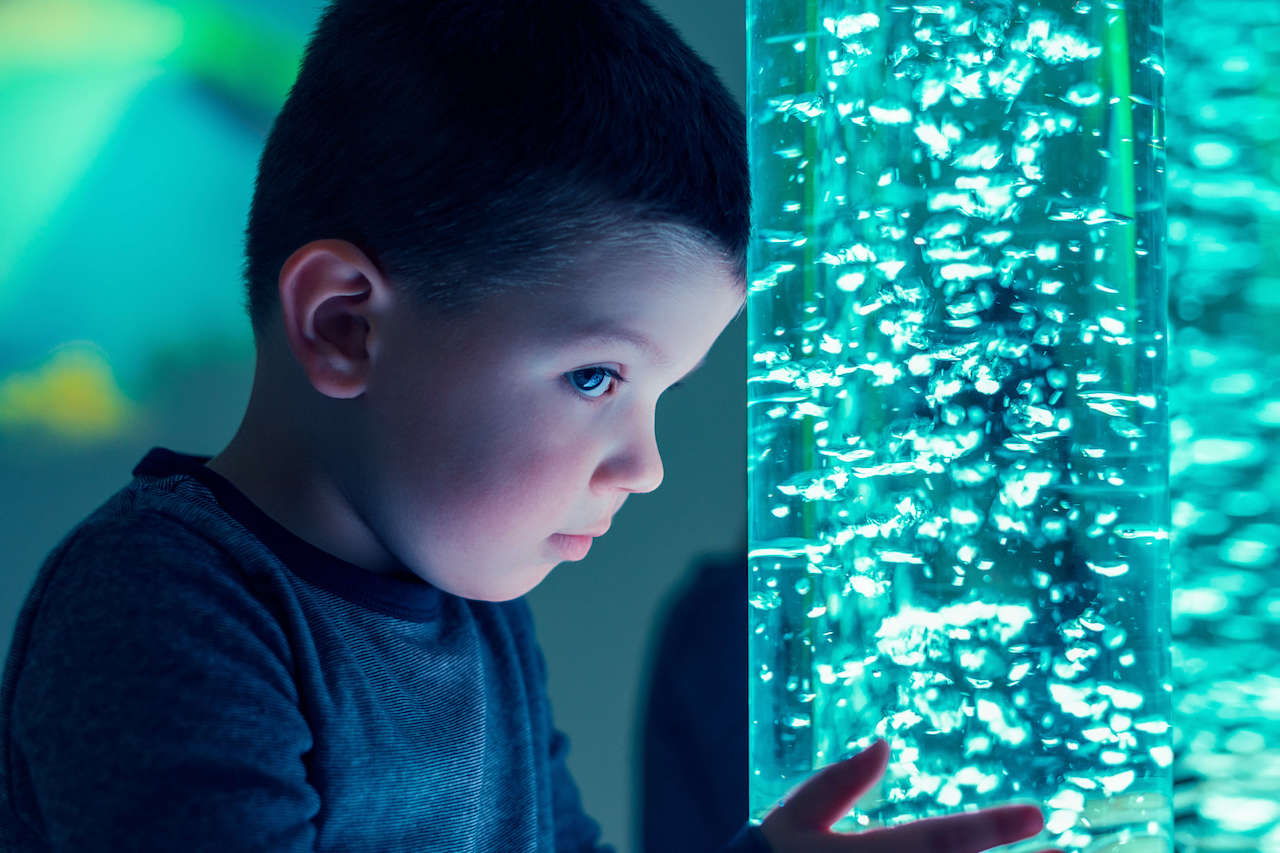 A child in a sensory stimulating room interacting with coloured light bubble as part of occupational therapy session