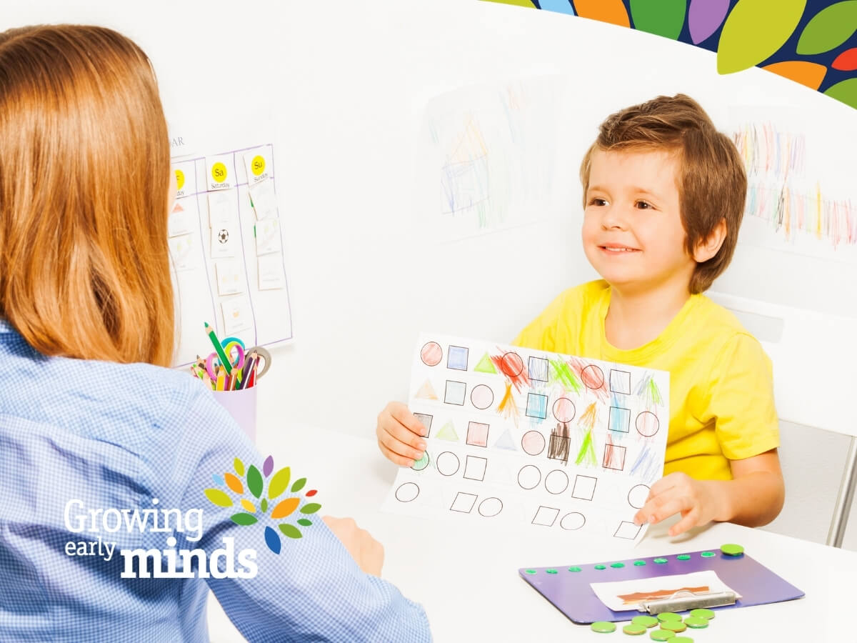 Picture of a child with ASD seated at a table with a therapist, working on an activity with shapes and colours