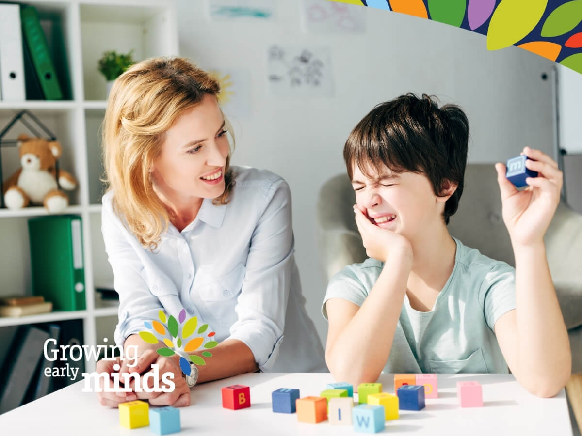 Image of a boy with ASD seated at a table with a woman and playing with blocks